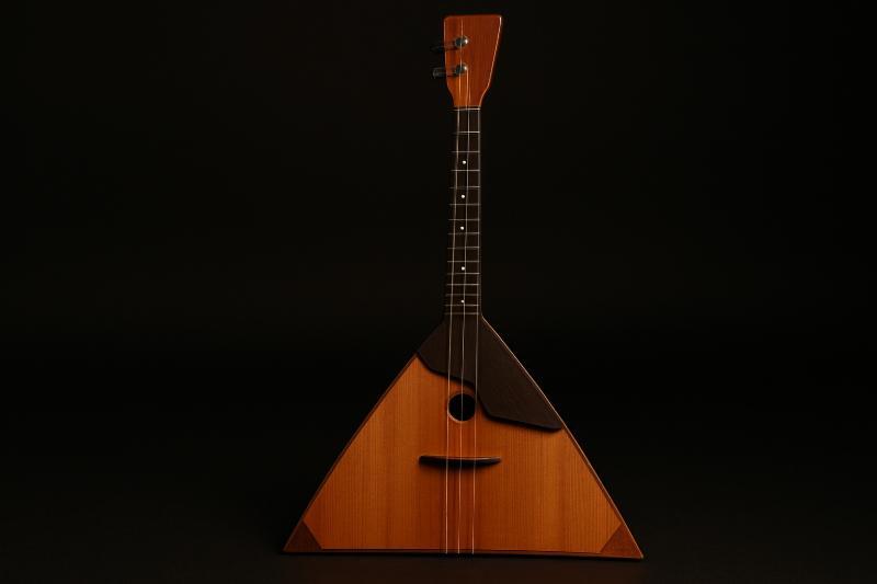 Russische Balalaika mit dreieckigem Holzkorpus und drei Saiten, freigestellt vor schwarzem Hintergrund