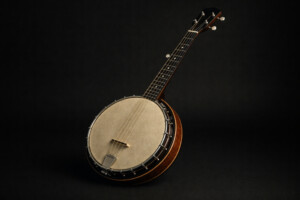 Fünfsaitiges Banjo mit rundem Metallkorpus, Holzgriffbrett und Stimmmechaniken, diagonal liegend auf schwarzem Hintergrund