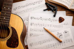 Akustikgitarre mit verstreuten kostenlosen Gitarrennoten, Plektrum und Kapodaster auf Holztisch