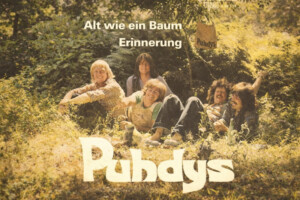 Vintage Albumcover der Puhdys: Fünf Männer sitzen entspannt im Grünen unter Bäumen, sonnige Stimmung, Schriftzug 'Alt wie ein Baum Erinnerung' im Vordergrund