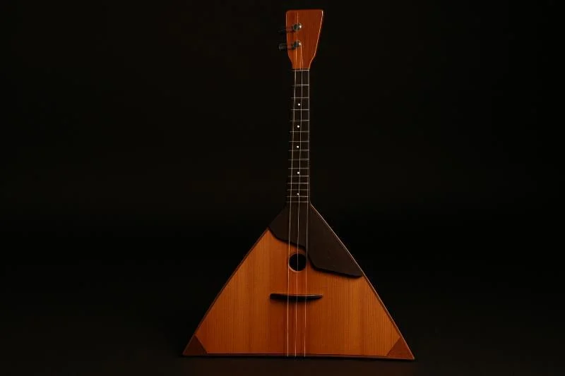 Russische Balalaika mit dreieckigem Holzkorpus und drei Saiten, freigestellt vor schwarzem Hintergrund